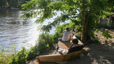 Im Licht der untergehenden Sonne sitzen Besucher im Open-Air-Bereich vom Veranstaltungsort Holzmarkt an der Spree.