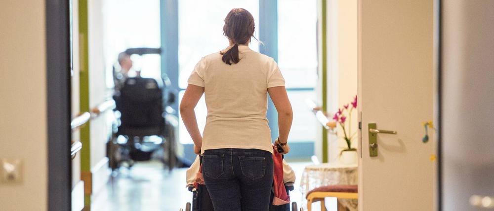 Eine Pflegerin schiebt eine Person im Rollstuhl.