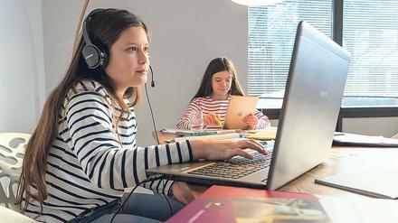 Zwei Mädchen sitzen im Homeschooling vor ihren Computern.