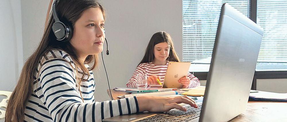 Zwei Mädchen sitzen im Homeschooling vor ihren Computern.