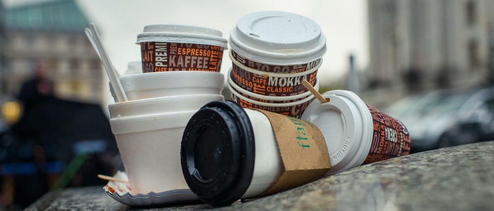 Einweg-Kaffeebecher und Plastikschalen stapeln sich an einem Gehweg.