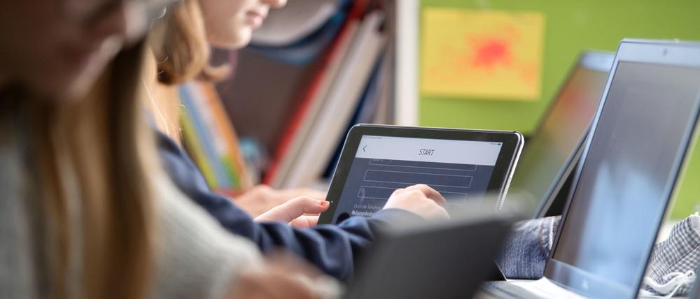 Schülerinnen und Schüler nehmen im Klassenzimmer einer 9. Klasse am Geografieunterricht mit Hilfe von Laptops und Tablets teil.