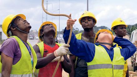 Hierarchien an der Elfenbeinküste. Ein chinesischer Ingenieur von PowerChina and Sinohydro, umringt von seinen einheimischen Mitarbeitern von Ci-Energies beim Bau einer Hochspannungsleitung im Distrikt Yopougon in Abidjan (2015).