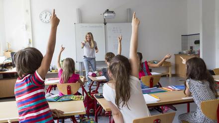 Eine junge Lehrerin interagiert in einem Klassenraum fröhlich mit einer kleinen Gruppe von Schülerinnen und Schülern.
