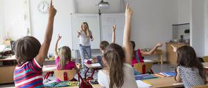 Eine junge Lehrerin interagiert in einem Klassenraum fröhlich mit einer kleinen Gruppe von Schülerinnen und Schülern.