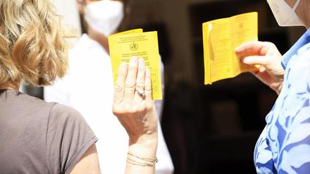 Zwei Frauen halten ihren Impfpass zur Kontrolle in die Luft.