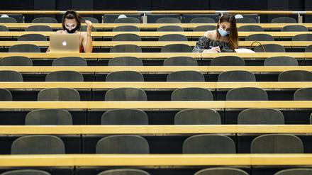  Studentinnen mit Mund-Nasen-Schutz sitzen in einem Hörsaal.
