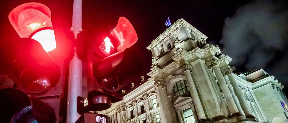 Eine rote Ampel leuchtet vor dem Reichstagsgebäude bei Nacht.