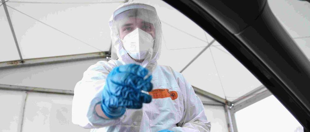 Ein Mitarbeiter einer Drive-In-Teststation will einen Nasen-Abstrich nehmen.