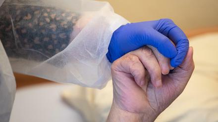 Eine Altenpflegerin in Schutzkleidung hält die Hand eines Bewohners. (Symbolbild)