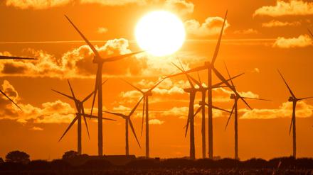 Die Sonne geht am Bredstedter Koog hinter einem Windpark mit Windrädern unter.