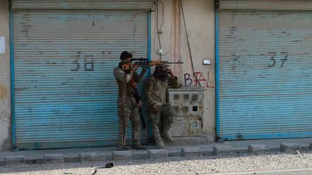 Zwei bewaffnete afghanische Sicherheitskräfte stehen auf einer Straße, auf der Patronenhülsen liegen und kämpfen mit Taliban.