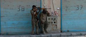 Zwei bewaffnete afghanische Sicherheitskräfte stehen auf einer Straße, auf der Patronenhülsen liegen und kämpfen mit Taliban.