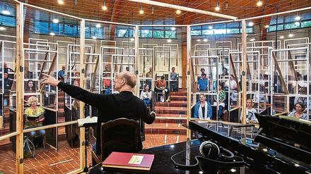 Übertragung. Chorchef Eberhard Friedrich dirigiert im Chorsaal die Sängerinnen und Sänger. Im Aufführungssaal wird Singen nur gemimt.