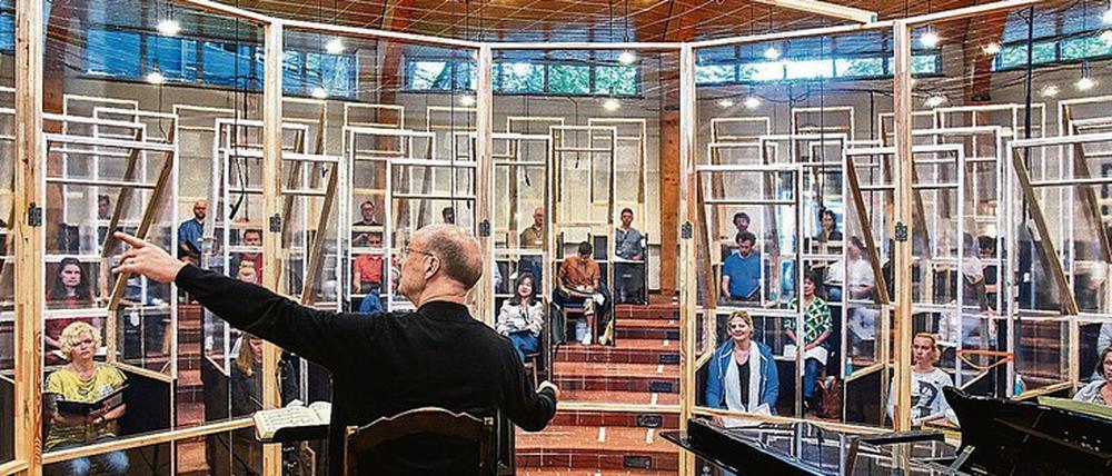 Übertragung. Chorchef Eberhard Friedrich dirigiert im Chorsaal die Sängerinnen und Sänger. Im Aufführungssaal wird Singen nur gemimt.