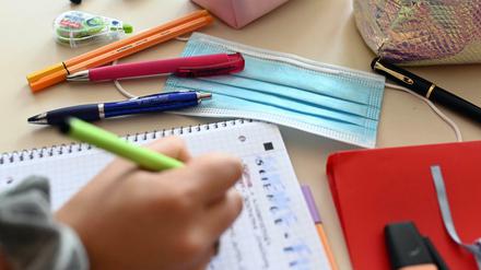 Zu sehen ist ein Arbeitstisch im Klassenzimmer, ein Kind schreibt in ein Heft.
