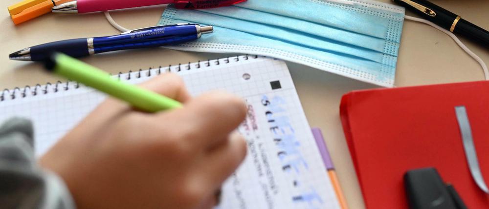 Zu sehen ist ein Arbeitstisch im Klassenzimmer, ein Kind schreibt in ein Heft.