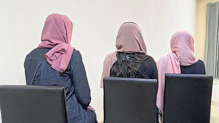 Drei Frauen mit Kopftüchern sitzen mit dem Rücken zur Kamera auf schwarzen Lehnstühlen.