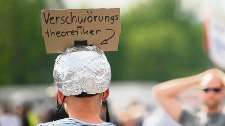 Mann mit Aluhut und Pappschild "Verschwörungstheoretiker".