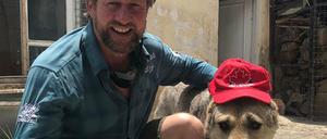 Paul Farthing kniet neben einem Hund, der eine Kappe trägt.