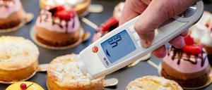 Ein Lebensmittelkontrolleur hält in einer Patisserie ein Thermometer an eine kleine Torte.