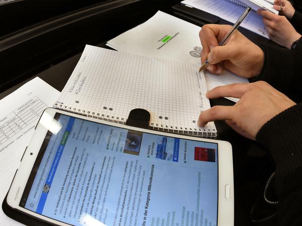 Studierende arbeiten in einem Hörsaal mit Tablet und Collegeheften.