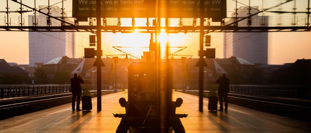 Fahrgäste sind am Hauptbahnhof bei Sonnenaufgang auf dem Bahnsteig zu sehen, wobei sich die Szenerie in einer Vitrine spiegelt.