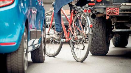 Lassen Sie mich durch. Eine Radfahrerin schlängelt sich auf dem zugeparkten Radweg zwischen zwei Autos hindurch. Archivbild