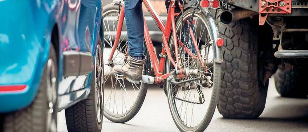 Lassen Sie mich durch. Eine Radfahrerin schlängelt sich auf dem zugeparkten Radweg zwischen zwei Autos hindurch. Archivbild