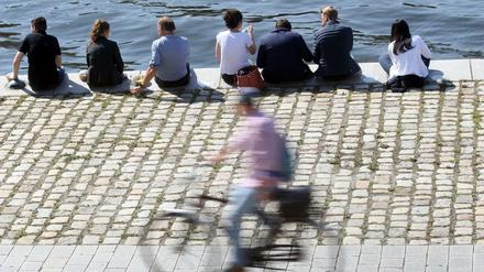 Menschen sitzen bei Temperaturen um 25 Grad Celsius am Ufer der Spree im Regierungsviertel und genießen die warme Herbstsonne, während ein Fahrradfahrer an ihnen vorbeifährt. Nach Angaben der Meteorologen wird auch in den kommenden Tage mildes Herbstwetter den Vorrang haben.