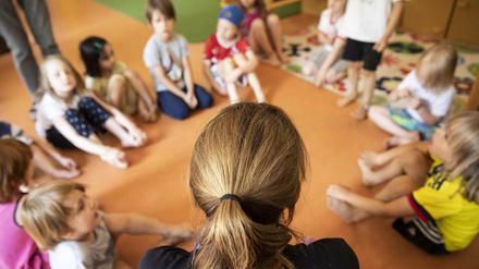 Erzieherin sitzt mit Kindern im Kreis auf dem Boden.