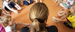 Erzieherin sitzt mit Kindern im Kreis auf dem Boden.