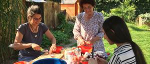 Die Freiwilligen vom Nachbarschaftsgarten Kreuzberg backen Pizza im selbstgebauten Steinofen und schneiden dafür Gemüse.