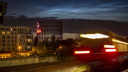 Dämmerung am Bahnhof Südkreuz, eine S-Bahn beleuchtet und verwischt, ein halb illuminierter Bürobau, im Hintergrund der Schöneberger Gasometer.