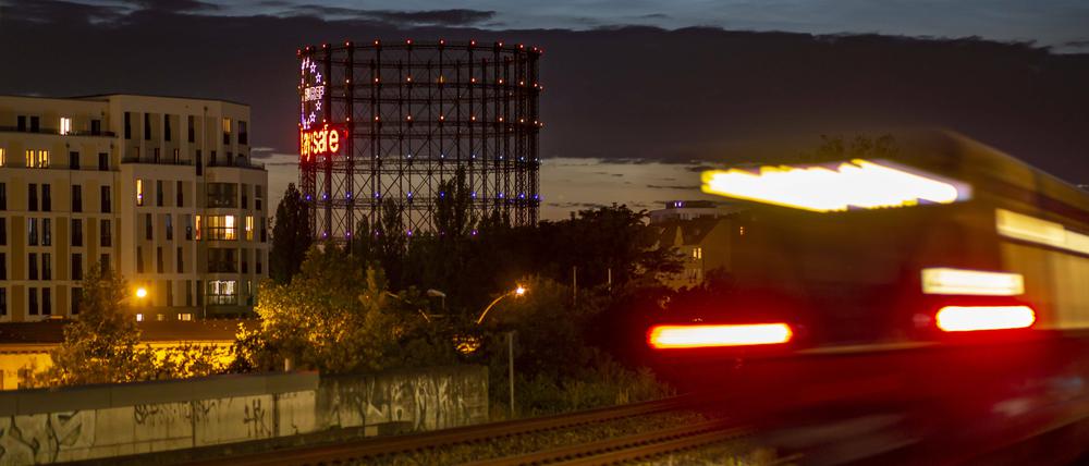 Dämmerung am Bahnhof Südkreuz, eine S-Bahn beleuchtet und verwischt, ein halb illuminierter Bürobau, im Hintergrund der Schöneberger Gasometer.