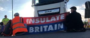 Zwei Männer sitzen vor einem Lastwagen und spannen einen Banner mit der Aufschrift "Insulate Britain".