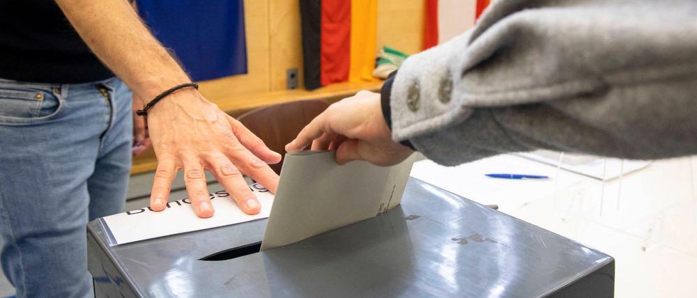 Stimmzettel-Einwurf in einem Berliner Wahllokal, im Hintergrund Europa-, Deutschland- und Berlin-Flaggen.