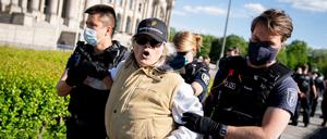 Eine Teilnehmerin wird von Polizeibeamten mit Mund-Nasen-Schutz vor dem Reichstagsgebäude am Rande einer Demonstration gegen eine Impfpflicht und gegen die freiheitseinschränkenden Maßnahmen der Bundesregierung im Rahmen der Ausbreitung des Coronavirus abgeführt.