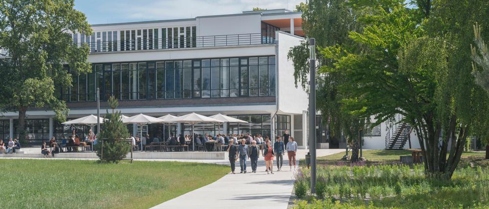 Sommerlich gekleidete Studierende und Lehrende gehen über den Campus der FU Berlin, im Hintergrund ein Mensagebäude.