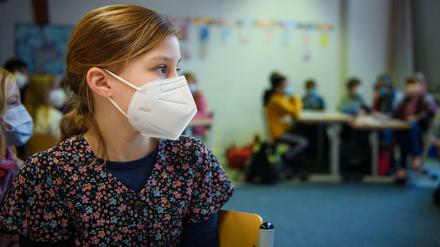 Grundschülerin mit FFP2-Maske sitzt im Klassenraum.