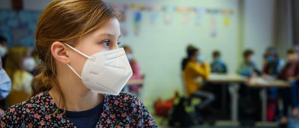 Grundschülerin mit FFP2-Maske sitzt im Klassenraum.