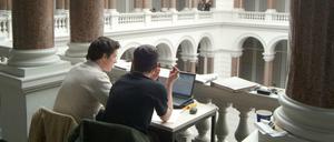 Im Kreuzgang des Lichthofs der TU Berlin sitzen zwei Studierende vor ihren Laptops nebeneinander an einem Tisch.