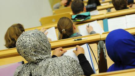 In einem Hörsaal sitzen zwei junge Frauen, die Kopftuch tragen.