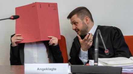 Die Angeklagte Jennifer W. hält auf ihrem Sitz im Gerichtssaal einen roten Aktendeckel vor ihr Gesicht.