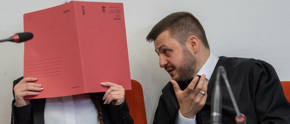 Die Angeklagte Jennifer W. hält auf ihrem Sitz im Gerichtssaal einen roten Aktendeckel vor ihr Gesicht.