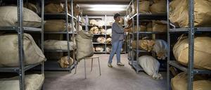 Prall gefüllte Stoff- und Papiersäcke liegen in einem Kellerraum in Metallregalen.