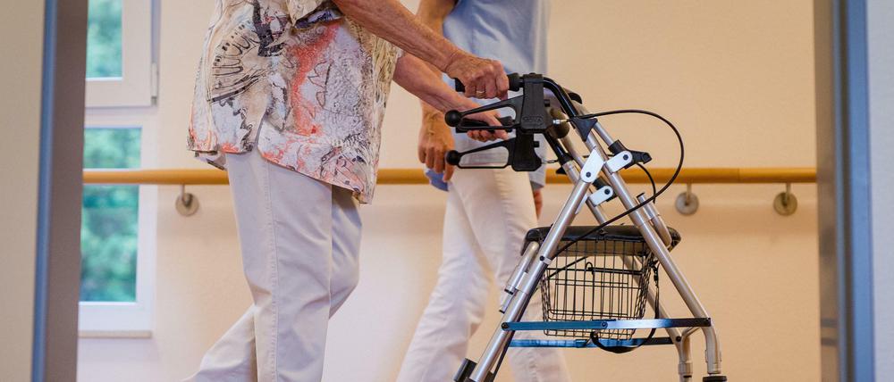 Eine Pflegekraft geht in einem Pflegeheim mit einer älteren Frau über einen Korridor. 