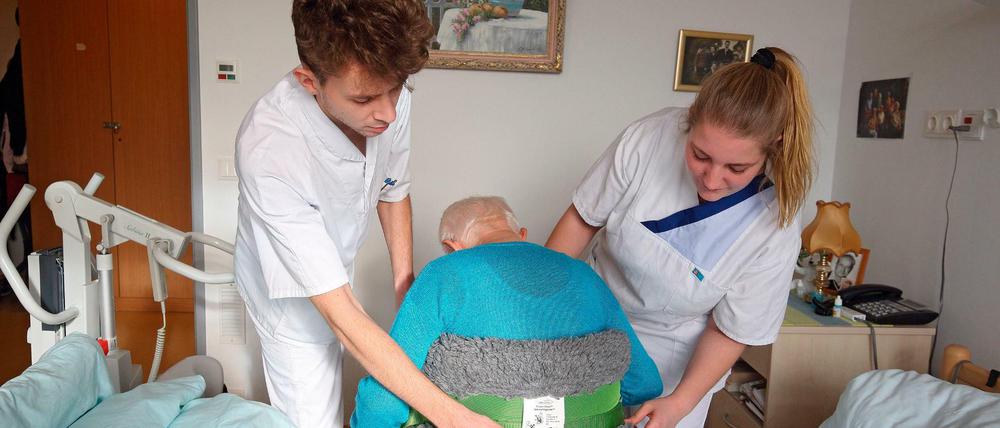 Zwei Auszubildende betreuen eine alte Frau am Krankenbett.