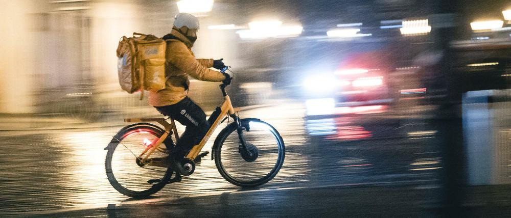 Ein Lieferbote auf einem Fahrrad fährt bei Regen durch Berlin. 