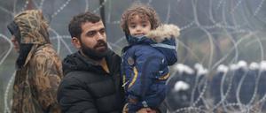 Ein Mann hält ein Kind und geht an einem Stacheldrahtzaun entlang an der belarussisch-polnischen Grenze. 